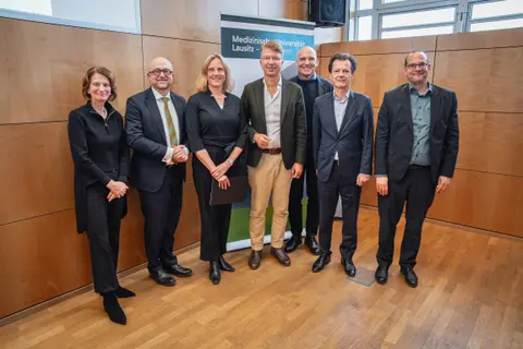 Sieben Personen stehen in einer Reihe und schauen lächelnd in die Kamera.