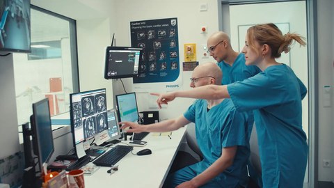 Drei Personen in blauen Kasacks zeigen und schauen auf einen Bildschirm mit Ultraschallaufnahmen von einem Herz.