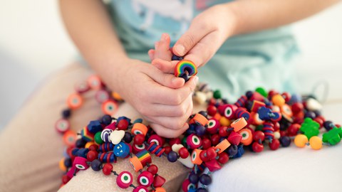Nahaufnahme von Kinderhänden, die zusammengebundene Mutperlen halten.