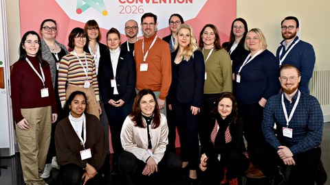 Eine Gruppe von Menschen vor einem Banner mit Text "NUM Convention 2026"