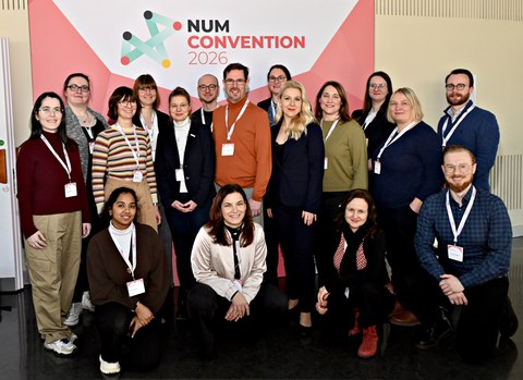 Eine Gruppe von Menschen vor einem Banner mit Text "NUM Convention 2026"