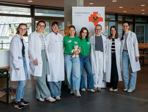 Eine Gruppe von jungen Menschen, teilweise in weißen Kitteln, stehen in einer Reihe und schauen in die Kamera.