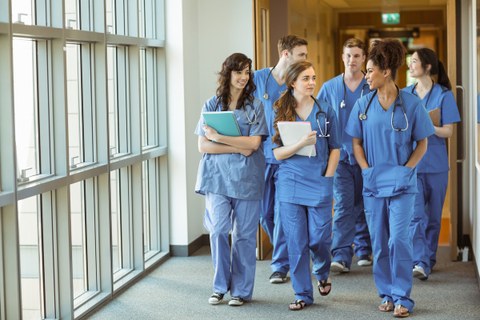 Auf dem Bild ist eine Gruppe Medizinstudenten zu sehen, die einen Flur entlanglaufen und dabei lachen und miteinander reden.