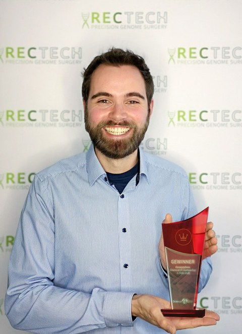 Felix Lansing präsentiert den Science4Life Preis, eine ca. 25 cm hohe Trophäe aus durchsichtigem und rotem Glas