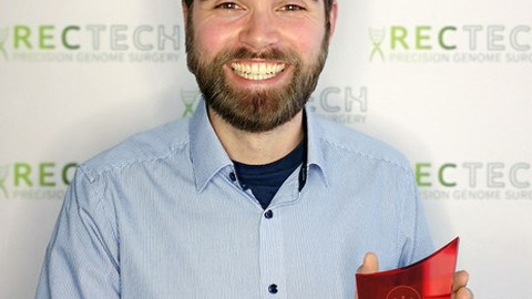 Felix Lansing präsentiert den Science4Life Preis, eine ca. 25 cm hohe Trophäe aus durchsichtigem und rotem Glas