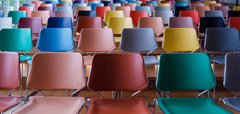 Verschiedenfarbige Stühle stehen aufgereiht in einem Raum.