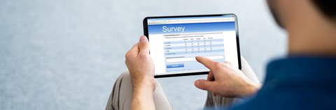 Eine Person hält ein Tablet in der Hand. Auf dem Bildschirm steht das Wort Survey.