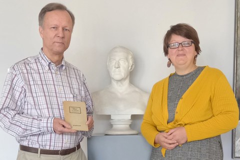 Ein Mann und eine Frau lächeln. Er hält ein Buch in den Händen.