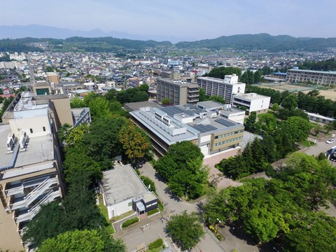 Campus der Shinshu University School Of Medicine in Matsumoto von oben. Im Hintergrund ist ein Gebirge.