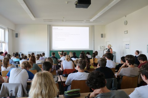 Hörsaal mit vielen Personen vor einer Präsentation 