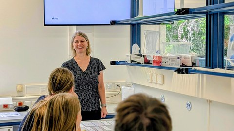 Frau hinter Schülern vor Monitor im Labor