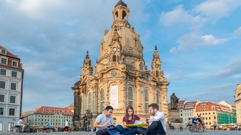 Foto: Drei junge internationale Leute sitzen in Dresden vor der Frauenkirche.