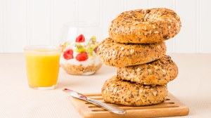 Auf dem Foto sieht man einen Stapel Bagels. Links daneben steht ein Glas Orangensaft. Im Hintergrund ist ein Glas mit Müsli, Joghurt und Früchten zu erkennen.