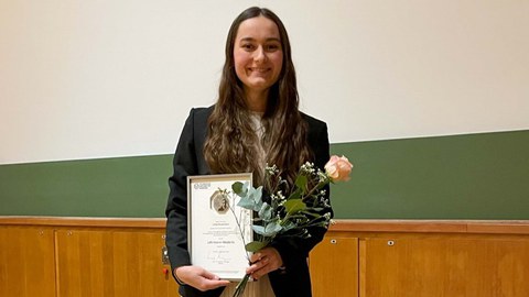 Brünette Frau mit rosa Rose und Auszeichnung in der Hand.