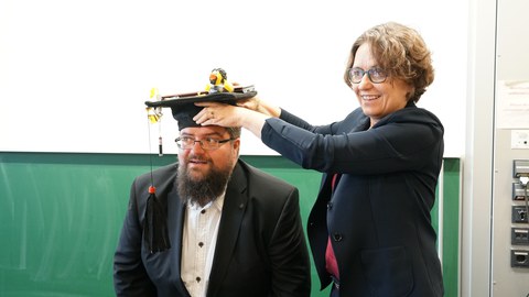 Woman puts PhD hat on man's hat