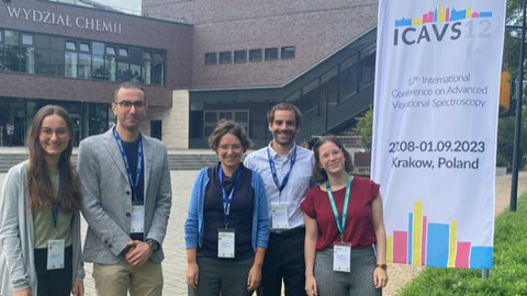 Drei Frauen und ein Mann stehen vor einem Gebäude und einem banner auf dem ICAVS12 steht. Die Menschen tragen Ausweise um den Hals.