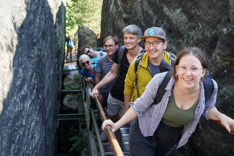 Zwei Frauen und vier Männer stehen hintereinander auf einer Treppe zwischen zwei Felsen