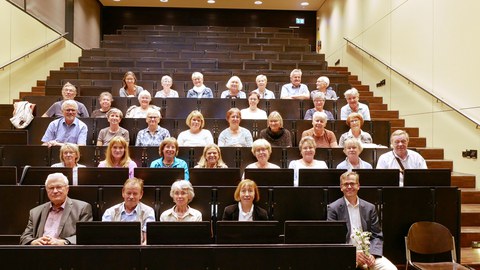 Frontalaufnahme von ca. 30 ehemaligen Studierenden, die in unteren Reihnen des Hörsaals sitzen