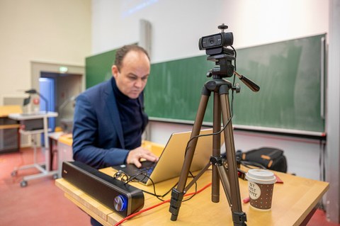 Foto eines Dozenten im Hörsaal, der am Laptop die Aufnahmen seiner digitalen Vorlesung speichert.