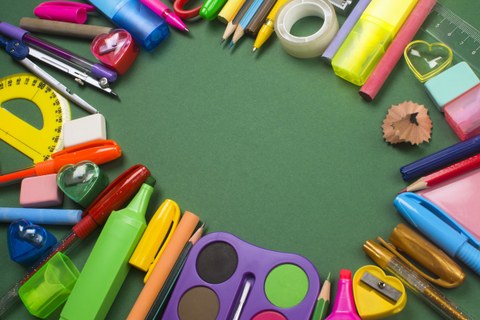 Auf dem Foto ist verschiedenes Schulmaterial, wie Stifte, Schere und Radiergummis zu sehen. Sie sind in einem Kreis zusammengelegt.