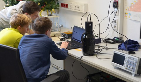 Jugendliche und ein Forscher sitzen vor einer Messanordnung