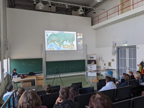 Schülergruppe in einem Hörsaal bei einer Videokonferenz