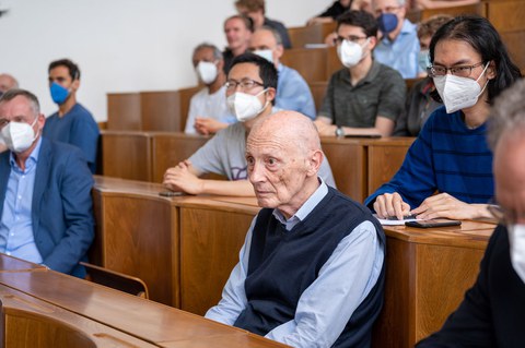 In einem Hörsaal sitzen mehrere Personen. Ganz vorne sitzt Professor Peter Fulde.
