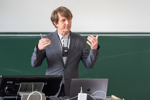 Ein Mann steht in einem Hörsaal mit dem Rücken zur Tafel.