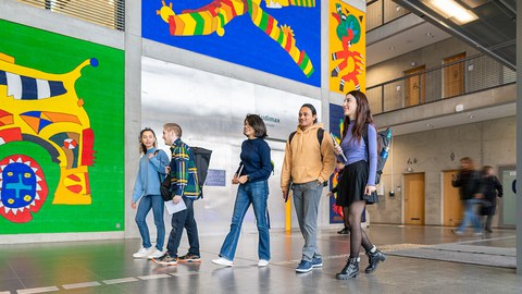 Photo of five students at TUD walking toward the “Audimax” while chatting.