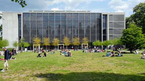 Rückseite des Hörsaalzentrum der TU Dresden. Auf der Wiese sitzen viele Studierende in kleinen Gruppen.