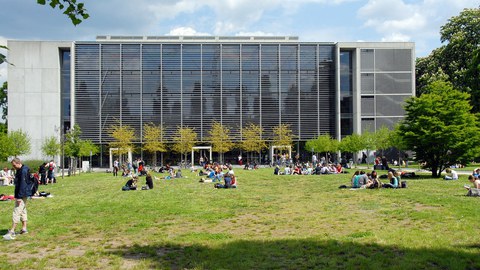 Rückseite des Hörsaalzentrum der TU Dresden. Auf der Wiese sitzen viele Studierende in kleinen Gruppen.