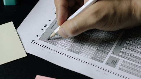 Eine Hand hält einen Stift in der Hand und korrigiert Werte auf einem Stück Papier.