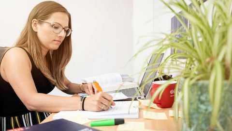 Eine Studentin arbeitet am Schreibtisch, füllt ein Notizheft aus. 