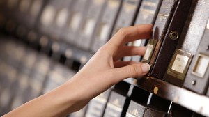 Foto: Die Hand einer Frau holt ein Buch aus einem Archivregal in einer Bibliothek.