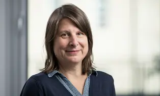 Portraitaufnahme einer Frau mit heller Haut und mittelbraunen, glatten, schulterlangen Haaren. Sie trägt einen dunkelblauen Pullover.