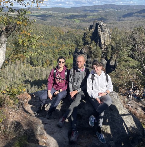 Kristina Rainich, Gael Cordero Otero und Jonathan Wehnert sitzen auf einem Berggipfel in der Sächsischen Schweiz.