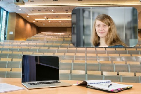 Blick vom Rednerpult, auf dem ein Laptop steht, in einen leeren Hörsaal, in dem ein Bild von Stefanie Schelinski eingefügt wurde