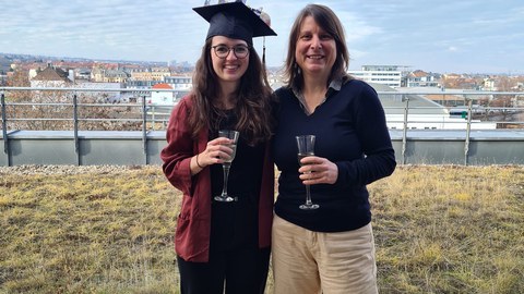 Lisa Jeschke trägt ihren Doktorhut und steht neben ihrer Betreuerin Prof. von Kriegstein