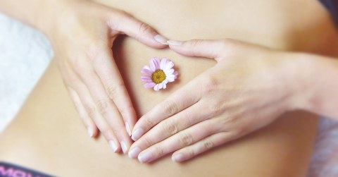 Eine Frau legt ihre Hände auf ihren Bauch. Im Bauchnabel steckt ein Gänseblümchen.