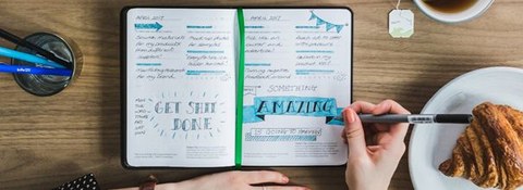 Draufsicht auf Schreibtisch mit ausgefüllten Kalender; Hände einer Person, die in Kalender schreibt