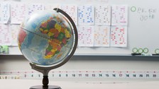 Das Foto zeigt einen Globus. Im Hintergrund befinden sich viele Zettel mit farbigen Markierungen an einem Whiteboard.