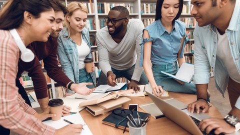 Foto von sechs Studenten aus verschiedenen Ländern, die zusammen in der Bibliothek fröhlich lernen.