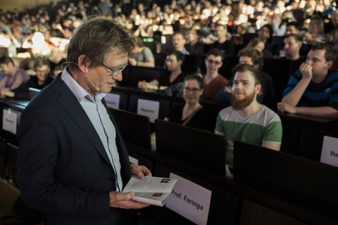 Ben Feringa mit einem Buch vor den gefüllten Reihen des Audimax