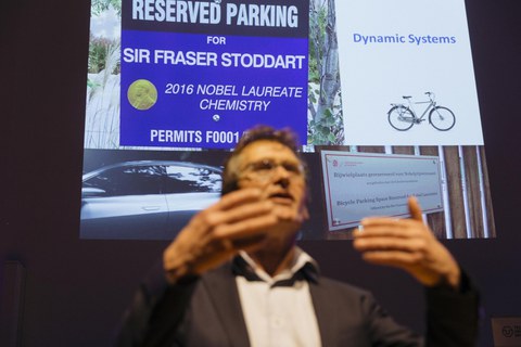 Ben Feringa bei seinem Vortrag vor einem seiner Slides, das eine Auto- und eine Fahrrad-Park-Plakette für Nobelpreisträger zeigt