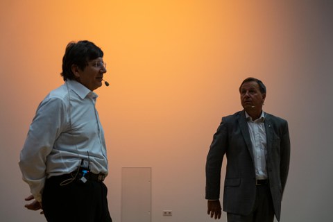Andre Geim und Clemens Kirschbaum vor einer orange beleuchteten Wand.
