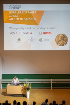 Prof. Dr. Angela Rösen-Wolff steht am Pult. Hinter ihr sind die Sponsoren der Veranstaltung angeworden.