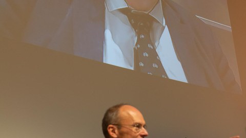 Prof. Dr. Carsten Timm ruft Fragen für Prof. Reinhard Genzel auf, der hinter ihm an die Wand projiziert wird