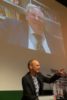 Prof. Dr. Carsten Timm ruft Fragen für Prof. Reinhard Genzel auf, der hinter ihm an die Wand projiziert wird