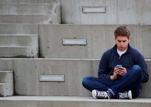 Jugendlicher sitzt auf einer Treppe mit Handy in der Hand.