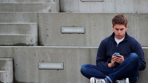 Jugendlicher sitzt auf einer Treppe mit Handy in der Hand.